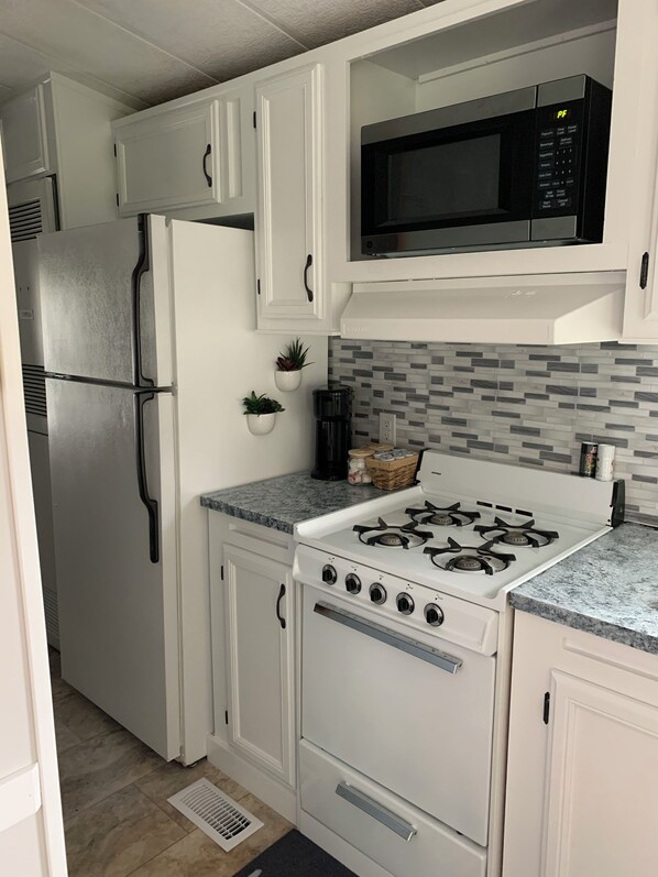 Una cocina con armarios blancos, un refrigerador de acero inoxidable, un microondas, una estufa a gas y un rebozado de azulejos.