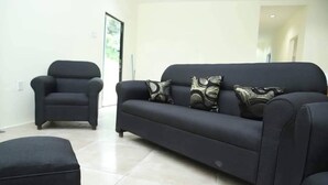 Un salon avec un canapé noir, un fauteuil noir et un pouf assorti.