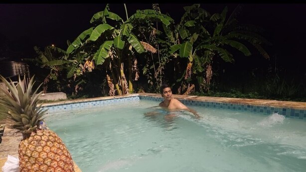 Une personne dans une piscine, avec un ananas et un objet emballé sur le bord.