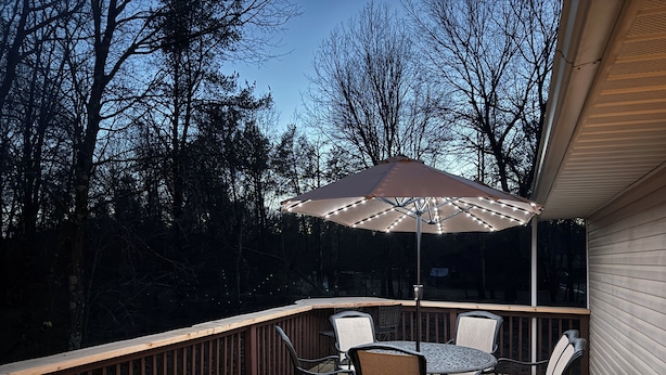 Una terraza de madera con una mesa, sillas, una sombrilla con luces y una barandilla.