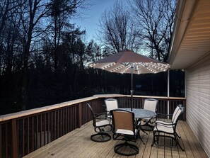 A wooden deck with a table and chairs, an umbrella with lights, and a railing. - Rustic Comfort Near Woods and Water (Necedah)