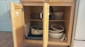 Un armario de madera con dos estantes, cada uno con utensilios de cocina.