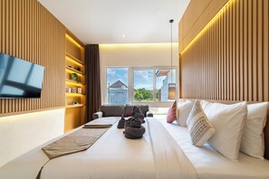 Quarto de hotel moderno com uma cama grande, televisão de tela plana na parede, prateleira embutida com objetos decorativos e vista para o exterior por grandes janelas.