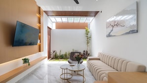 Una sala de estar moderna con un televisor de pantalla plana montado en una pared de madera, un sofá color beige, una mesa de centro redonda y un gran ventanal con luz natural.