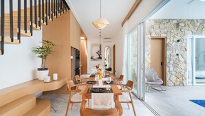Un área de comedor moderna con una mesa y sillas de madera, una escalera con escalones de madera y un muro de piedra con una puerta que da a una zona de piscina.
