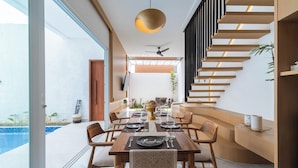 Un comedor moderno con una mesa de madera dispuesta para cuatro personas, una escalera con escalones de madera y vista a una piscina.