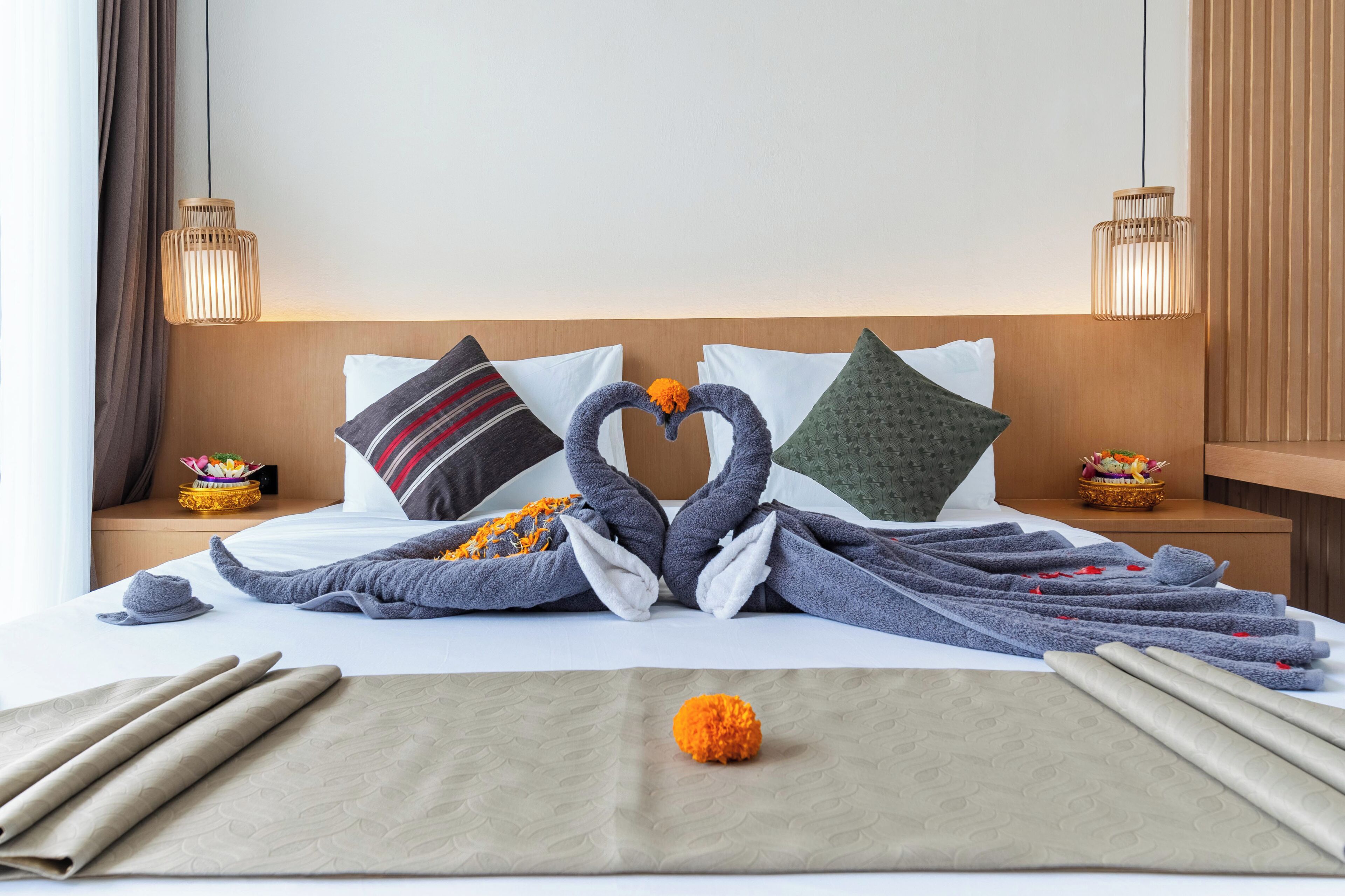 A neatly made bed with towels arranged in a swan shape, a decorative orange pom-pom, and a folded beige towel on the bed.