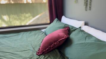 A bed with green bedding and a red pillow, a book on the bed, and a window with a view of trees.