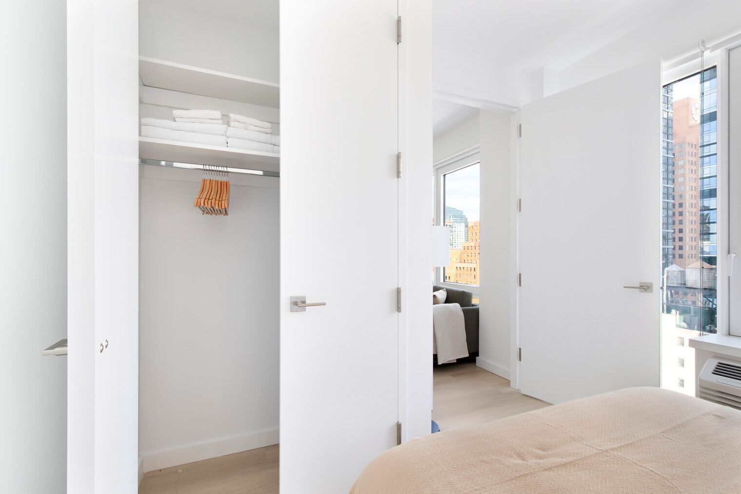 A modern hotel room with a large window, a walk-in closet, and a view of the cityscape.