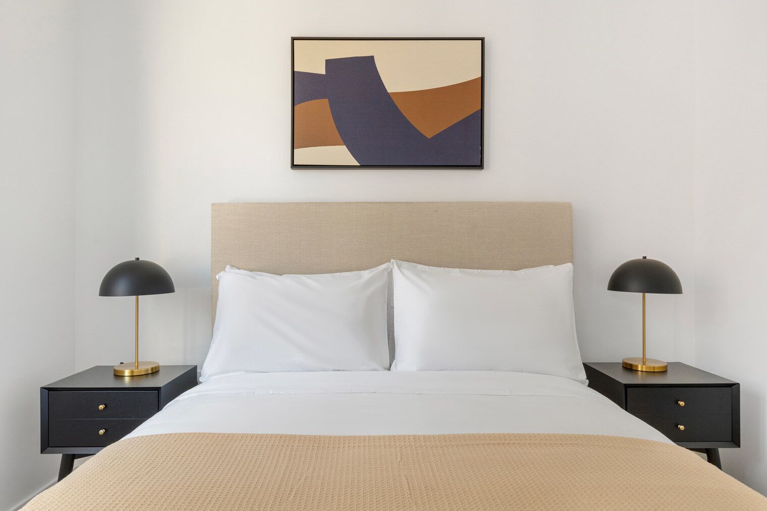 A neatly made bed with white linens, two bedside tables with lamps, and a modern abstract painting on the wall.