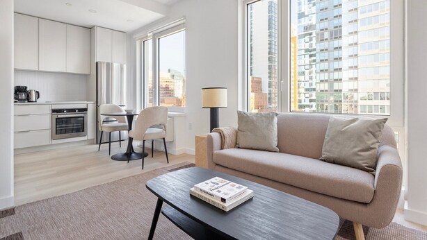 Un appartement moderne comprenant une cuisine, un coin repas et un salon. Il est doté de grandes fenêtres, d’un canapé et d’une table basse.