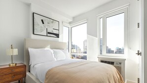 A modern bedroom with a large bed, a nightstand, a wall-mounted lamp, and a city view through large windows. - Blueground | Downtown Brooklyn, rooftop, nr Brooklyn Bridge (New York)