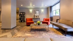 A modern lobby with a central coffee table, two red armchairs, a beige sofa, and a bookshelf. - Blueground | Downtown Brooklyn, rooftop, nr Brooklyn Bridge (New York)