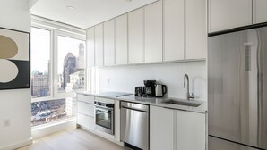 A modern kitchen with white cabinetry, stainless steel appliances, and a city view. - Blueground | Downtown Brooklyn, rooftop, nr Brooklyn Bridge (New York)