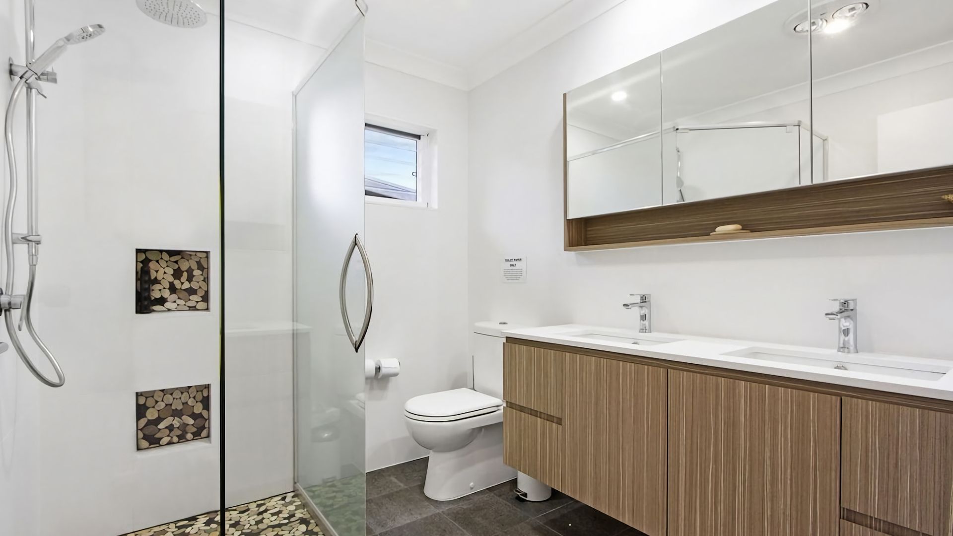 Een moderne badkamer met een glazen douchecabine, een toilet en een wastafel met spiegel.