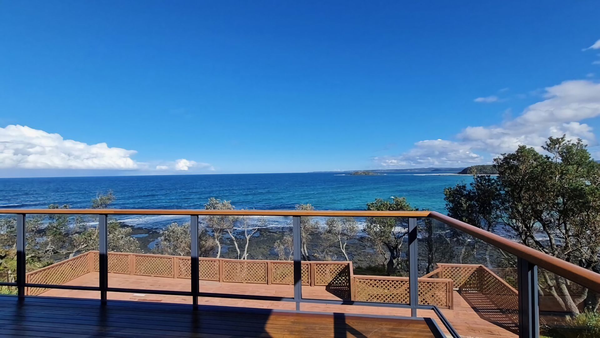 A wooden deck with a railing overlooking a coastal view.