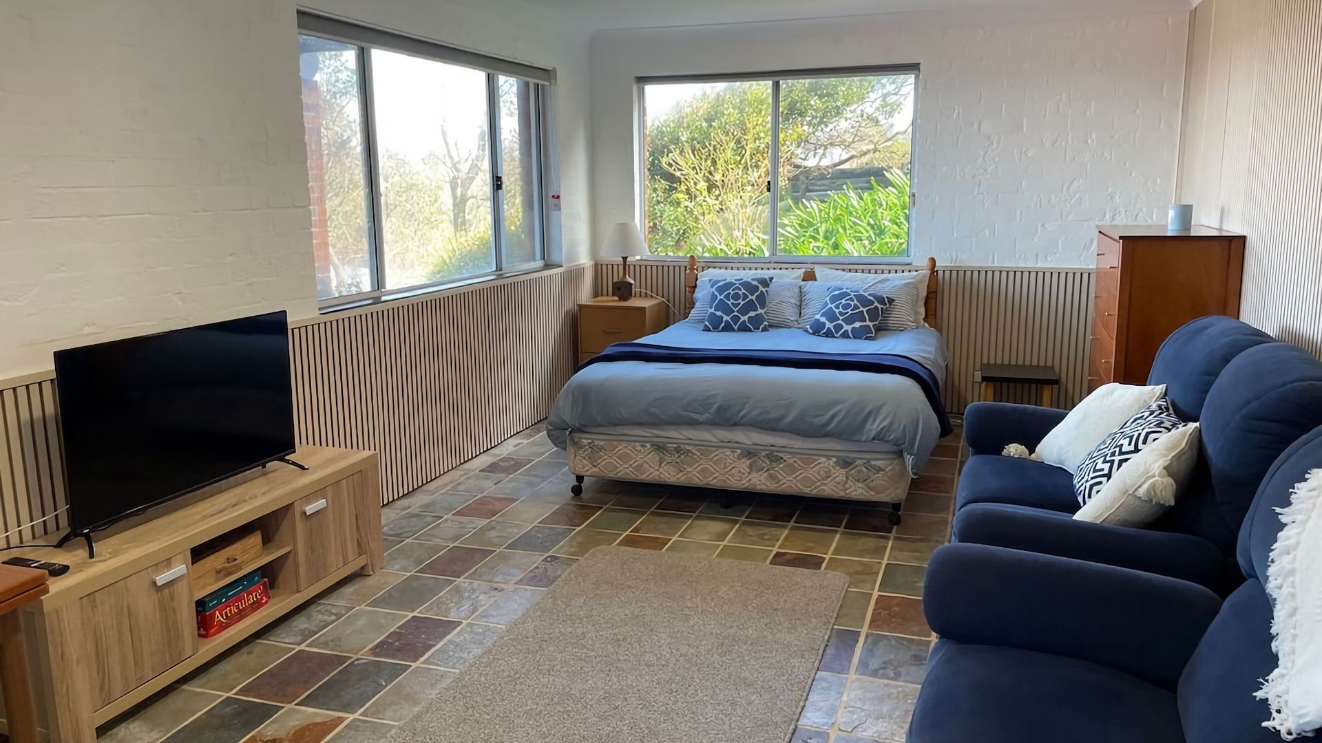 A bedroom with a bed, a TV, a sofa, and a window.