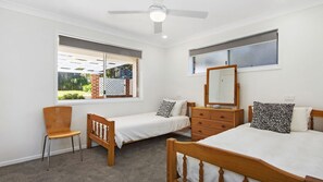 A bedroom with two single beds, a wooden dresser, a chair, a ceiling fan, and a window with a view of greenery. - Bellevue overlooking the ocean (Manyana)
