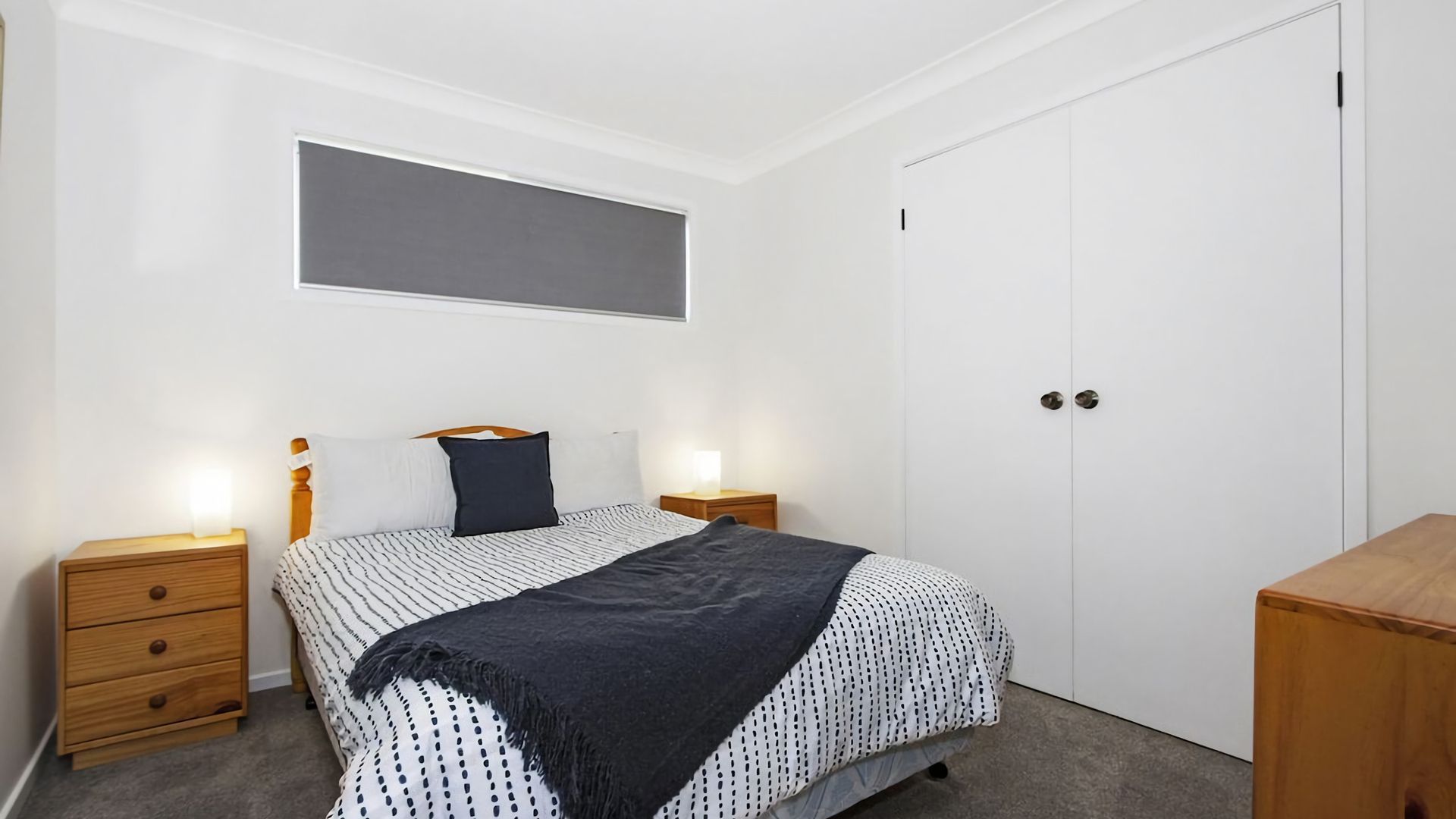 Ein Schlafzimmer mit einem Bett, zwei Nachttischen, einem Kleiderschrank und einem Fenster mit Jalousien.