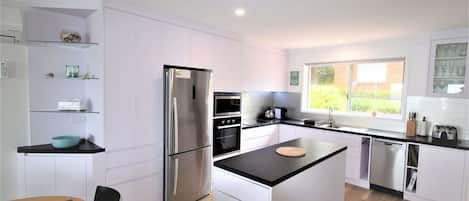 A modern kitchen with white cabinetry, a stainless steel refrigerator, an oven, and a built-in dishwasher.