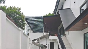 Uma piscina ao ar livre moderna com um escorregador em espiral, um brinquedo flutuante vermelho e verde, e uma escadaria que leva a um nível superior.