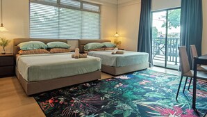 Quarto de hotel com duas camas, um ventilador de teto, uma janela grande com persianas, uma varanda com vista e um tapete estampado com flores.