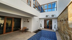 A modern two-story house with a large glass door, a small patio with a chair, and a tiled pool area. - Danka Luxury Villa (Batam)