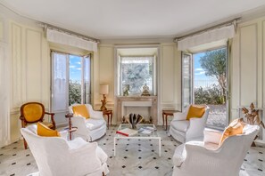 Un salon spacieux doté d’une cheminée, de grandes fenêtres et offrant une vue sur l’extérieur.