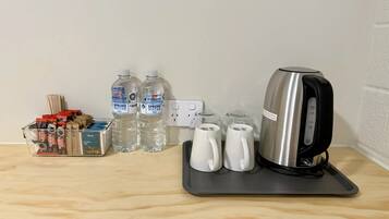 Een kitchenette met een waterkoker, twee waterflessen, een koffiezetapparaat en een doosje theezakjes.