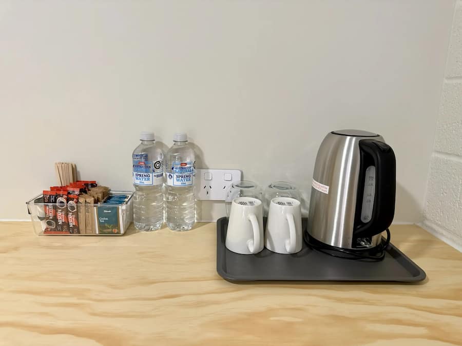 Een kitchenette met een waterkoker, twee waterflessen, een koffiezetapparaat en een doosje theezakjes.
