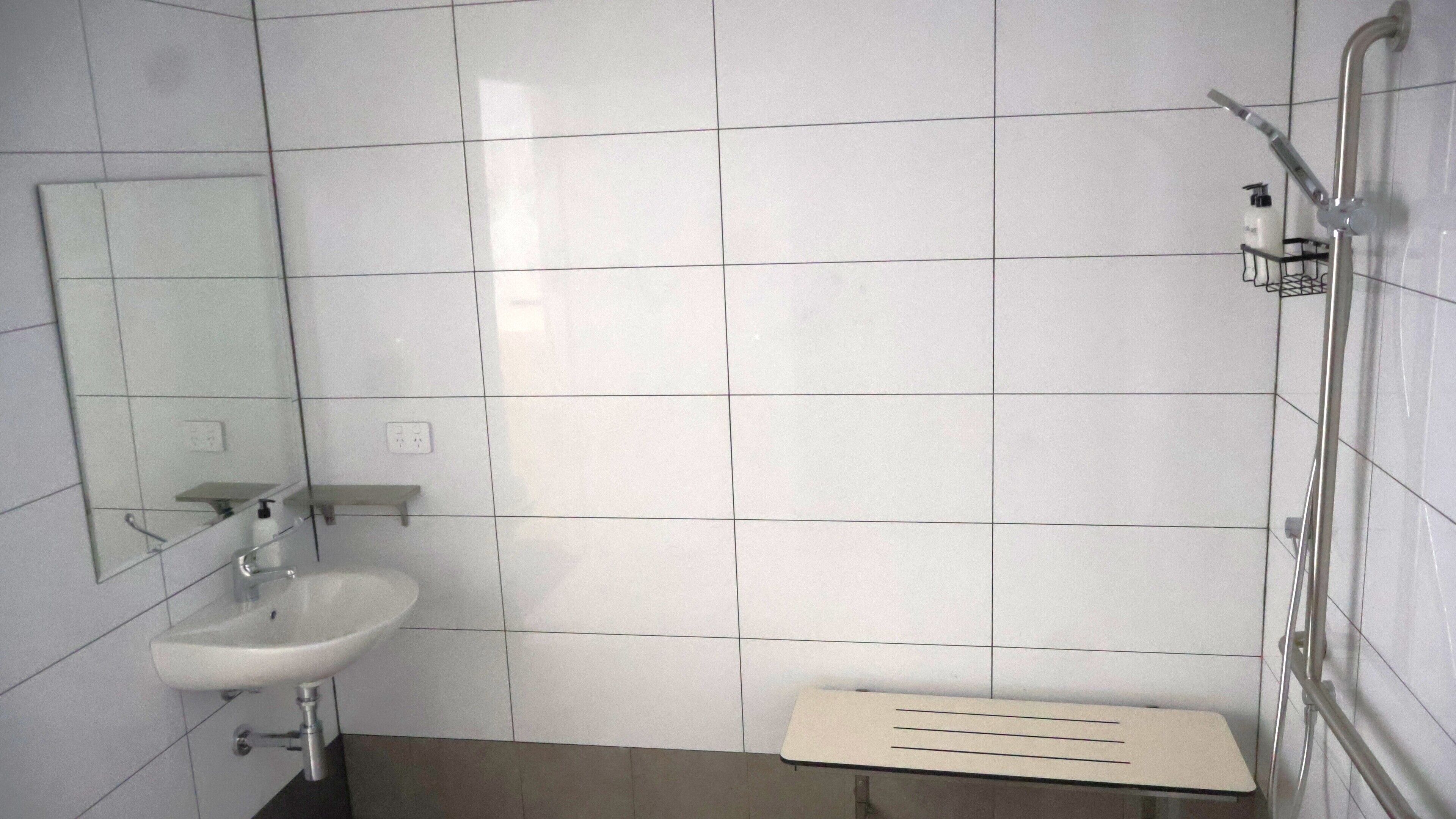 Une salle de bain avec des murs recouverts de carreaux blancs, un lavabo, un miroir et un espace douche.