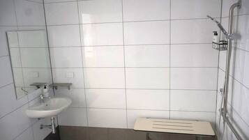 Une salle de bain avec des murs recouverts de carreaux blancs, un lavabo, un miroir et un espace douche.