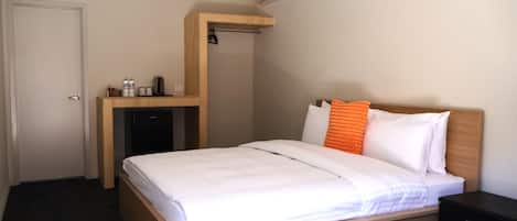 Ein Hotelzimmer mit einem Bett, einem kleinen Schreibtisch mit Kühlschrank, Wasserspender und Kaffeemaschine.
