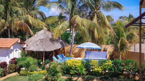 Ein tropisches Resort mit einer strohgedeckten Hütte, einem Poolbereich und üppiger Vegetation.