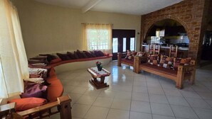 Ein geräumiges Wohnzimmer mit einer großen Couch, einer hölzernen Bank und einem kleinen Tisch. Es gibt eine Küchenzeile mit einem Backsteinbogen und einem Esstisch mit Stühlen.