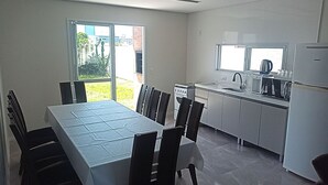 Una cocina moderna con electrodomésticos blancos, un comedor con mesa y sillas, y un ventanal corredero que da a un patio.