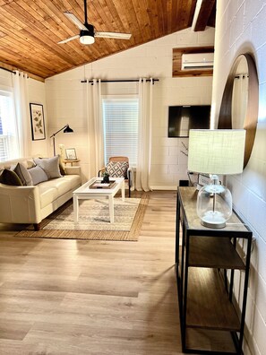 A living room with a white sofa, a coffee table, a lamp, and a TV. - The Twin Gables / Peaceful Cottage-feel 2 bedroom (Waco)