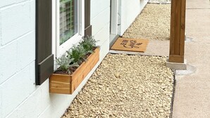 A building with white exterior walls, dark shutters, and wooden planters with greenery. - The Twin Gables / Peaceful Cottage-feel 2 bedroom (Waco)