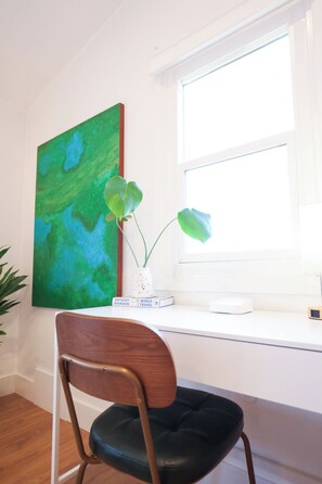Ein Zimmer mit Schreibtisch, Stuhl, Fenster und einem Gemälde.