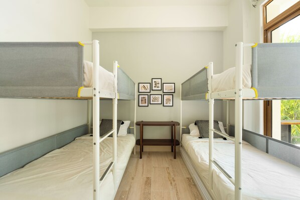 A dormitory room with bunk beds, a small table, and framed pictures on the wall.