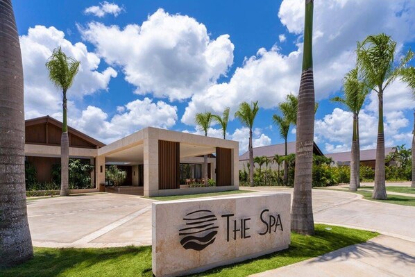 Un complejo de spa con un edificio central, palmeras y un cielo despejado.