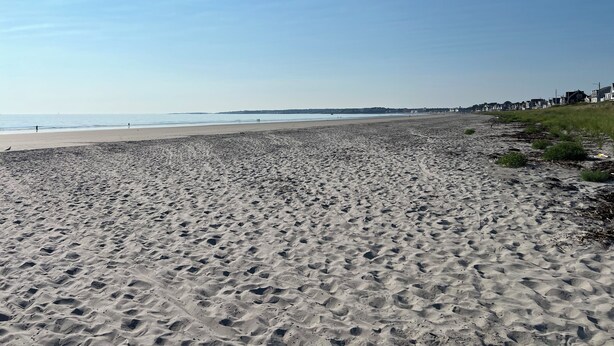 Une vaste plage de sable, parsemée d’empreintes, et un ciel dégagé.