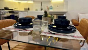 Une table à manger dressée avec des assiettes, des bols et des verres, avec une cuisine en arrière-plan.