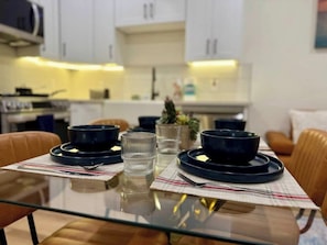 A dining table set with plates, bowls, and glasses, with a kitchen in the background.