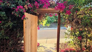 Une entrée en forme de pergola en bois, avec un chemin menant à une route.