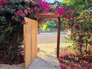 A wooden pergola entrance with a pathway leading to a road.