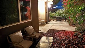 Un espace extérieur aménagé avec des chaises en osier et une table en verre, entouré d’un jardin où poussent des fleurs rouges et agrémenté d’une table de patio.