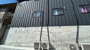 A building with a dark facade, multiple windows, and air conditioning units installed on the ground.