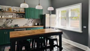 A modern kitchen with green cabinets, a wooden table, and pendant lights. - Forrest House Victor Harbor (Victor Harbor)
