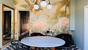 A dining area with a round table, black chairs, and a wall mural featuring flamingos and palm leaves. - Forrest House Victor Harbor (Victor Harbor)